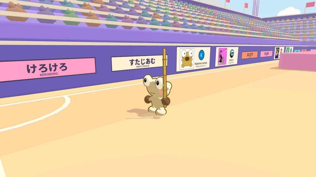 The west side wall of Kero Stadium under the packed stands. A row of panels with drawings hangs along the wall beside the advert boards, and Kero walks along the pitch.